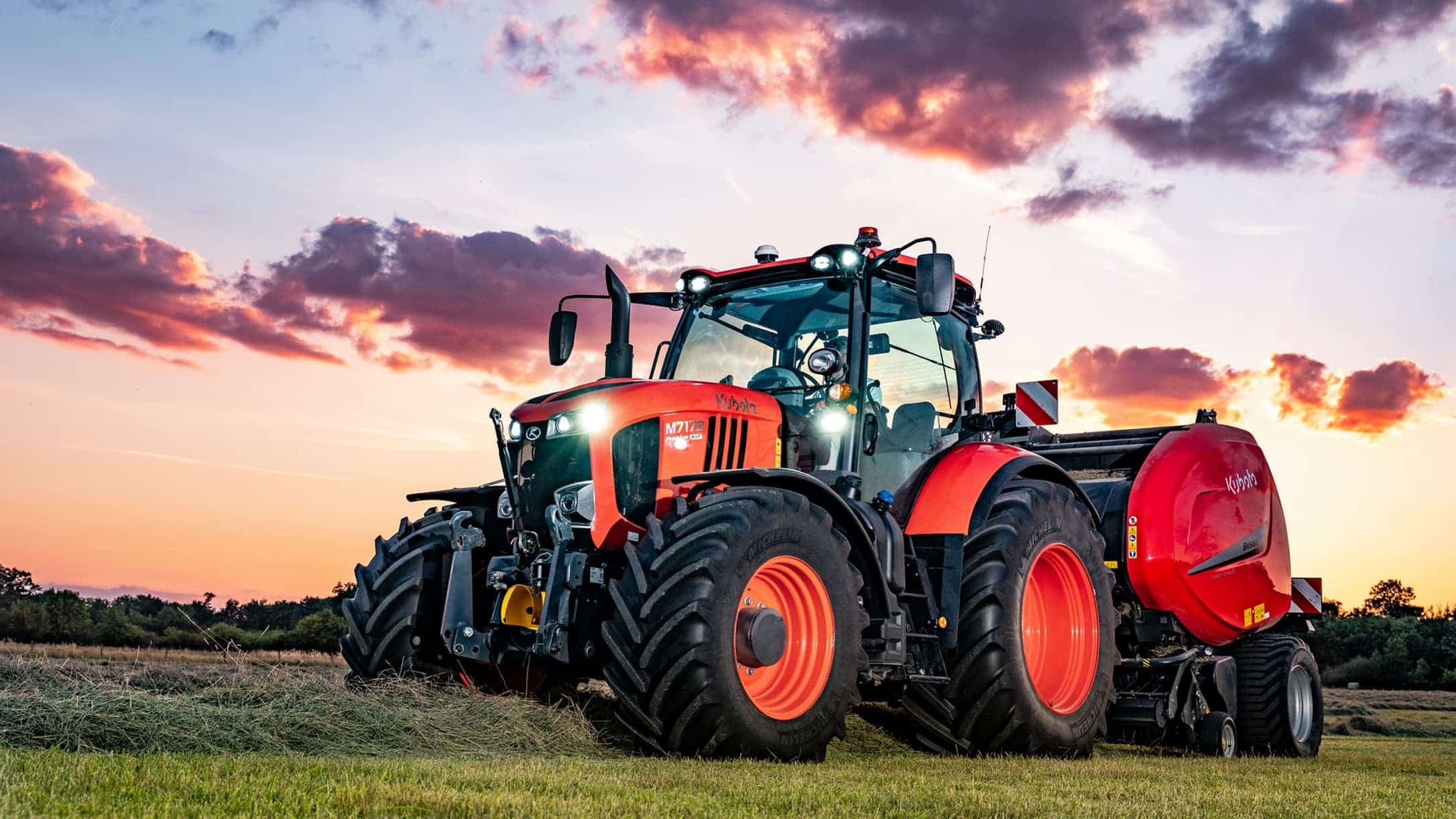 Kubota M7 tractor with baler at sunset